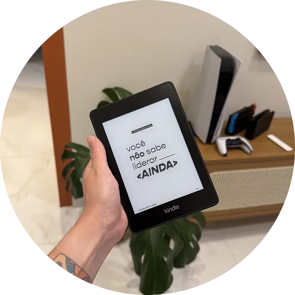 Pessoa segurando um Kindle que exibe a capa do livro “Você não sabe liderar ainda”. Ao fundo, há um ambiente moderno com um móvel e plantas, destacando a versão digital do livro.